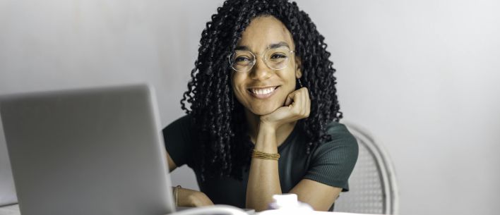 Happy ethnic woman sitting at table with laptop